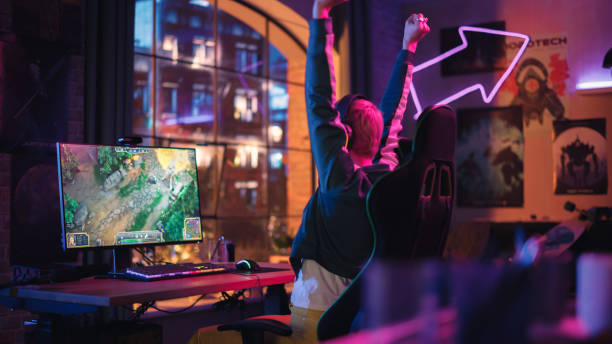 successful female gamer playing and winning in pvp rpg strategy video game in which players fight in a tournament on personal computer. stylish young woman celebrating victory in cozy room at home. - 电竞 個照片及圖片檔