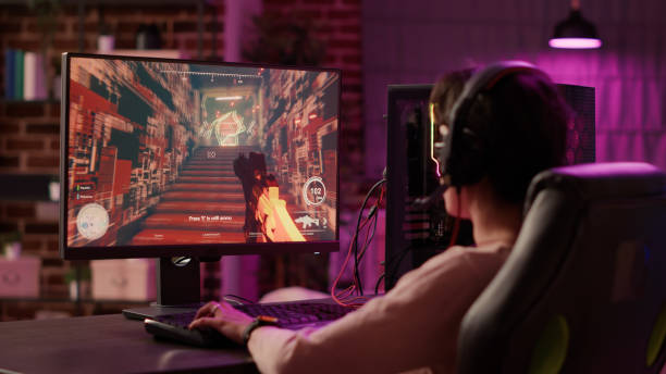 over shoulder view of gamer girl using pc gaming setup relaxing playing multiplayer online action video game - 电竞 個照片及圖片檔