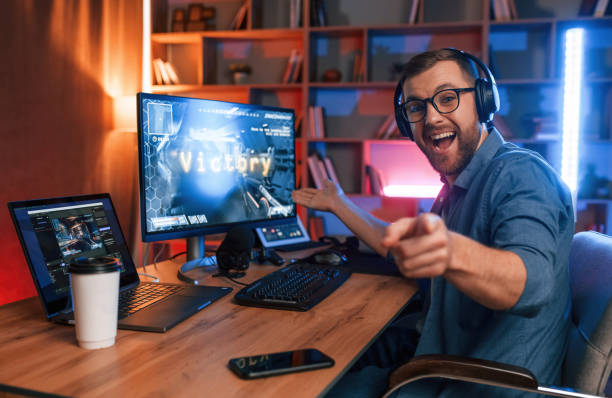 uplifting and energized man is playing the shooter game on his computer. neon lighting - 电竞 個照片及圖片檔