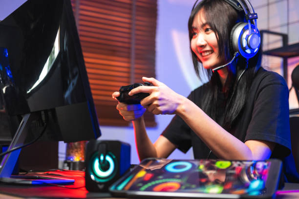 happy asia girl gamer wear headphone competition play video game online with computer colorful neon light in living room at night - 电竞选手 個照片及圖片檔